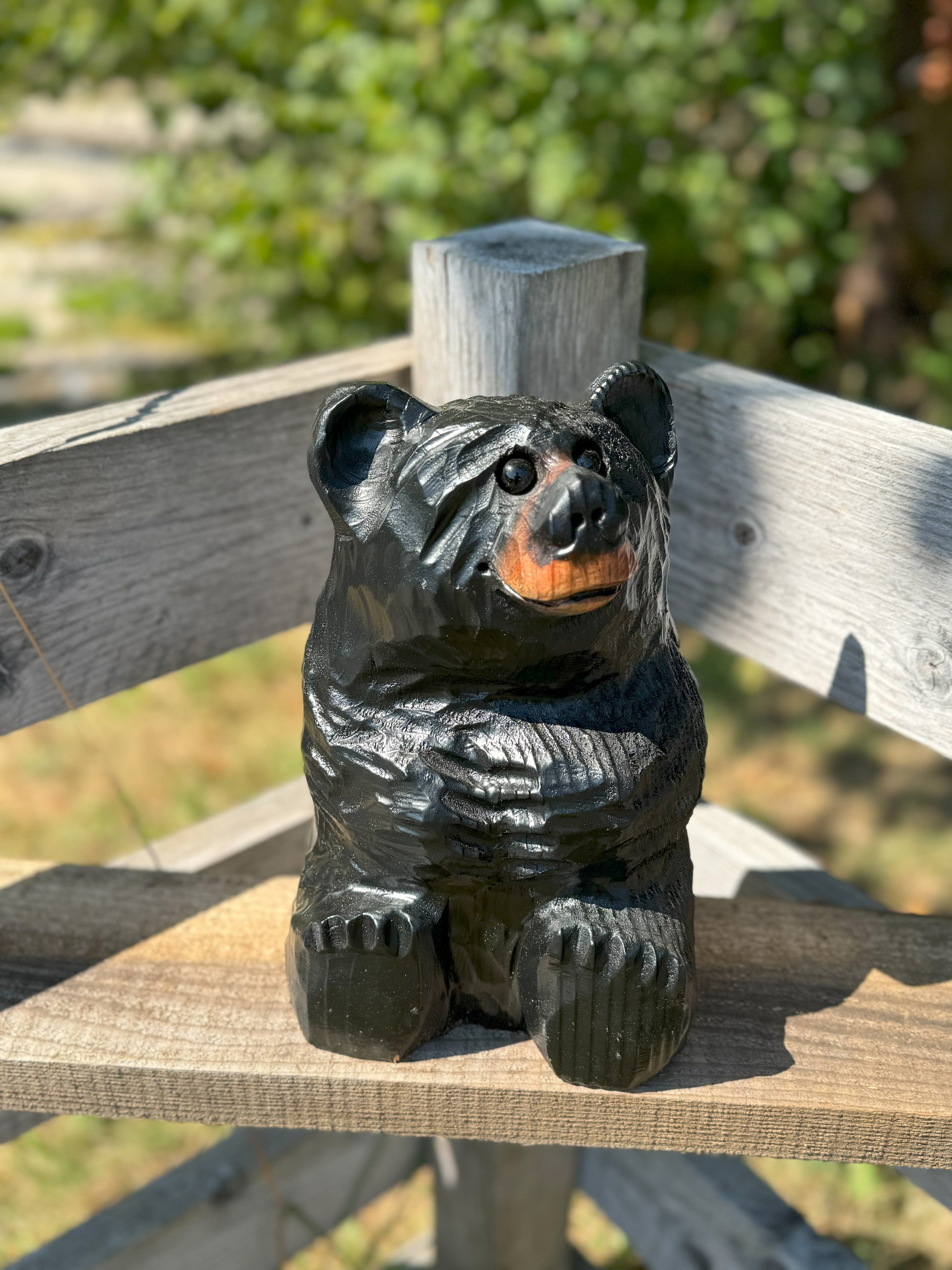 Black bear figurine sitting on a wooden bench with a blurred natural background